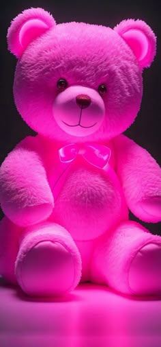 a bright pink teddy bear with a bow tie on it's chest sitting in front of a black background