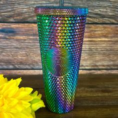 a colorful cup with a straw in it next to a yellow flower on a wooden table