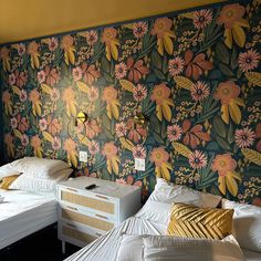 two beds in a room with floral wallpaper on the walls and white bedding