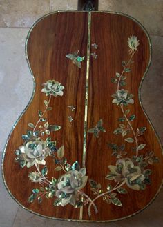 the back side of an acoustic guitar with flowers and leaves painted on it's sides