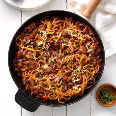 a skillet filled with spaghetti and meat on top of a white table next to two bowls