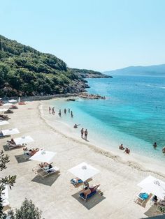 people are on the beach and in the water near some umbrellas, chairs and trees