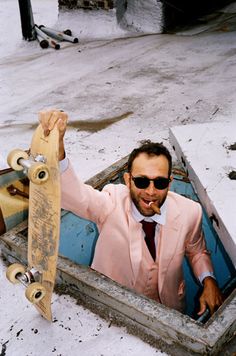 a man in a pink suit and tie holding a skateboard up to his face