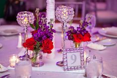 the centerpieces are decorated with red roses and purple flowers in glass vases