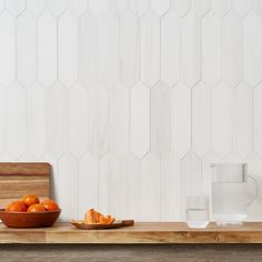 a bowl of oranges on a wooden table next to a glass of water and a cutting board