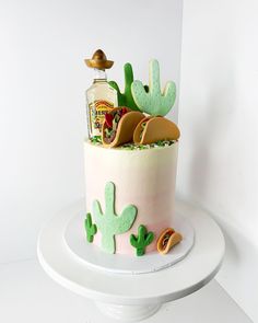 a birthday cake decorated with cactus decorations and condiments on a white pedestal against a white wall