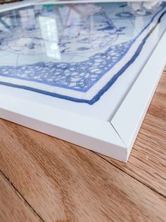 a close up of a piece of art on a wooden floor with white frame and blue border