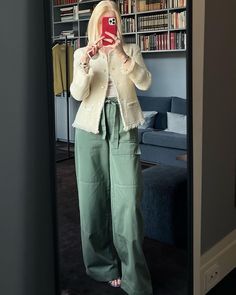 a woman taking a selfie in front of a bookshelf while wearing green pants