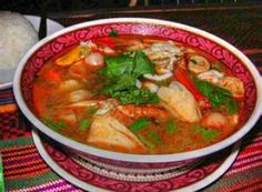 a red and white bowl filled with soup on top of a colorful table cloth next to a plate