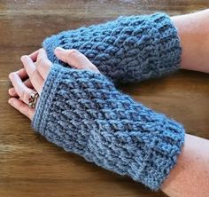 a woman's hand wearing a blue knitted arm warmer on top of a wooden table