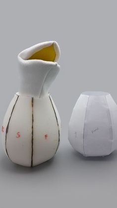 two white vases sitting next to each other on a gray surface, one with yellow top