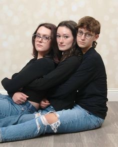 three young people sitting on the floor hugging each other with their arms around one another