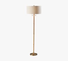 a gold floor lamp with a white shade on the base and a beige drum light