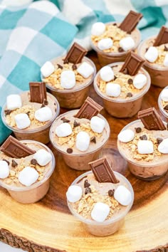 desserts with marshmallows and chocolate are arranged on a wooden platter