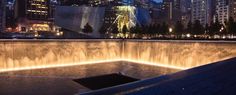 the city skyline is lit up at night, with water cascading in front of it