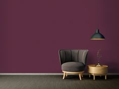 a chair and table in front of a purple wall with a black lamp hanging over it