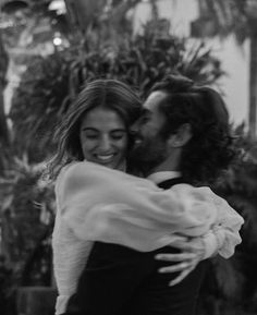 black and white photograph of a man hugging a woman in front of some plants with his arms around her