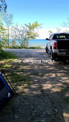 a truck parked next to a tent on the side of a road near trees and water