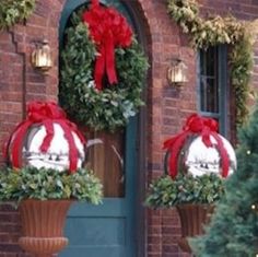 two christmas wreaths on top of large urns in front of a brick building