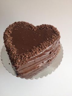 a heart - shaped chocolate cake on a glass platter with a white surface behind it