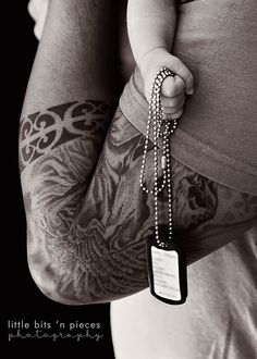 a person with tattoos on their arms holding a dog tag in his left hand and chain attached to the arm