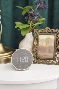 an alarm clock sitting on top of a white table next to a vase with purple flowers