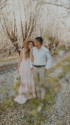 a man and woman standing next to each other in front of some trees with leaves