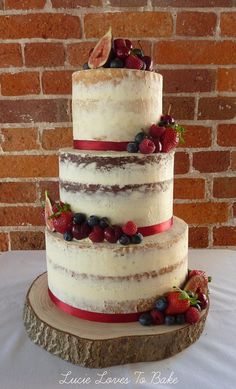 a three tiered cake with fresh berries on the top is displayed in front of a brick wall