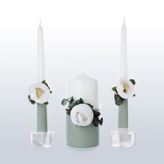 three white candles with flowers on them are sitting next to each other