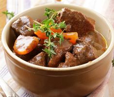 a brown bowl filled with meat and carrots on top of a table next to a fork