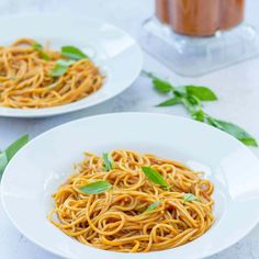 two white plates filled with spaghetti on top of a marble table next to a jar of tomato sauce