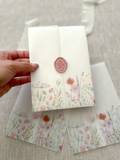 a hand holding an envelope with flowers on it and a wax stamp in the middle