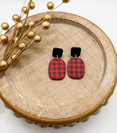 the red and black plaid earrings are sitting on a wooden tray