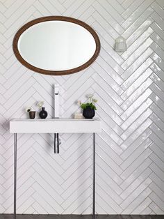 a white sink sitting under a round mirror next to a wall mounted faucet