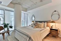 a bedroom with white walls and wood flooring has a large bed, two mirrors on the wall