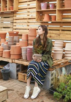 a woman sitting on a bench holding a potted plant in front of stacks of pots