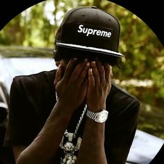 a man covering his face with his hands while wearing a supreme hat and bracelets