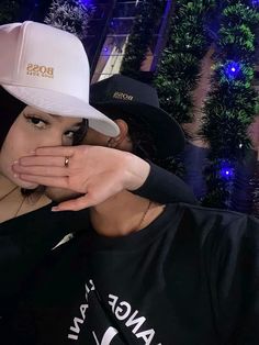 a woman covering her mouth while standing next to a man in a black shirt and white hat