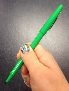 a person is holding a green pen with designs on it and has their thumb in the other hand