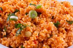 a close up view of rice and vegetables in a white bowl with green garnishes