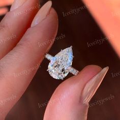 a woman's hand holding an engagement ring with a pear shaped diamond on it