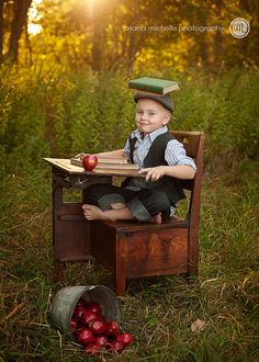 a young boy sitting in a chair with apples on top of his head and an apple basket next to him