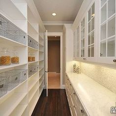 a long narrow kitchen with white cabinets and shelves filled with glass doors on both sides