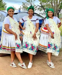 three women standing next to each other in front of a car wearing white dresses and green head wraps