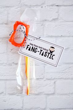 an orange pair of scissors in a plastic bag on a white brick wall with a tag