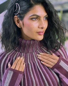 a woman with long black hair wearing a purple striped sweater and holding her hands on her chest