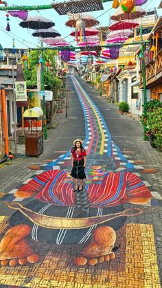 a woman standing in the middle of a street with an artistic mural on it's side