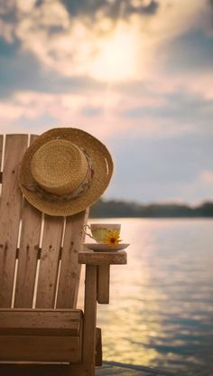 a wooden chair sitting on top of a beach next to the ocean with a hat on it