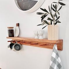 there is a clock on the wall above a shelf with pots and mugs next to it