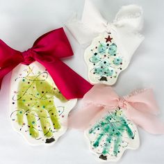 three handprinted christmas ornaments with bows on them